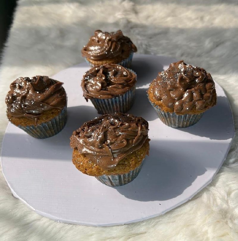 Five cupcakes with chocolate icing on a white board