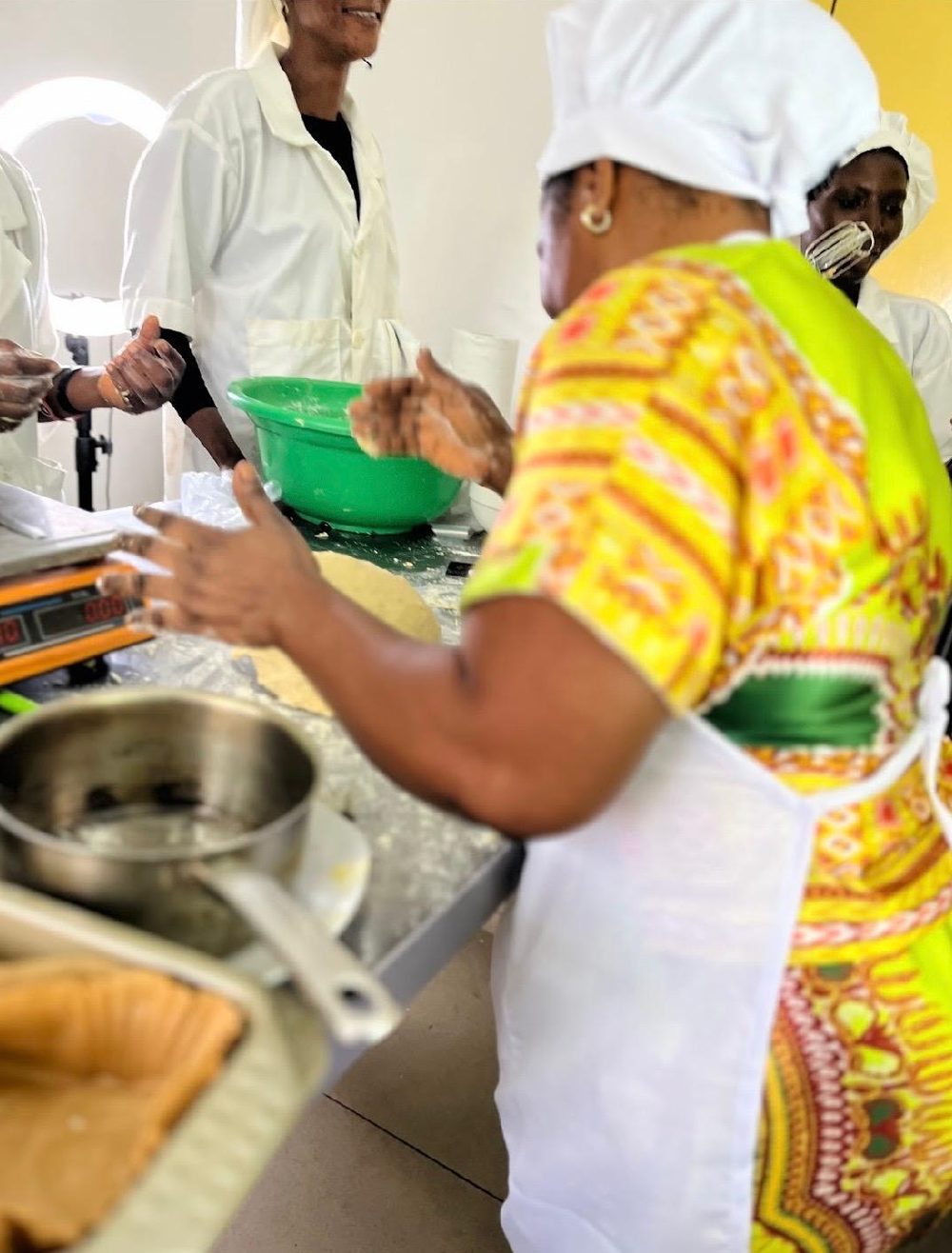 Women in white kitchen uniforms shaping dough together in a training kitchen