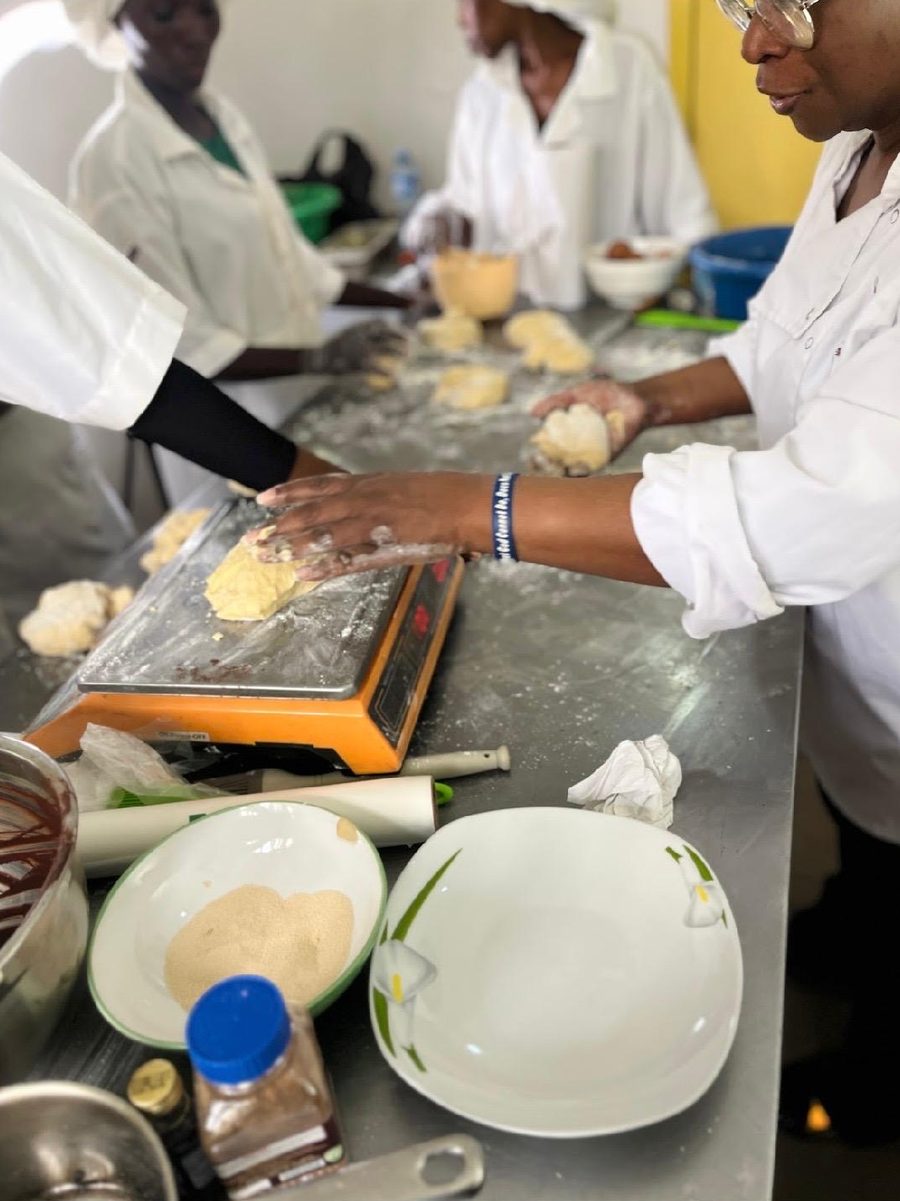 Women kneading and shaping dough at a steel counter